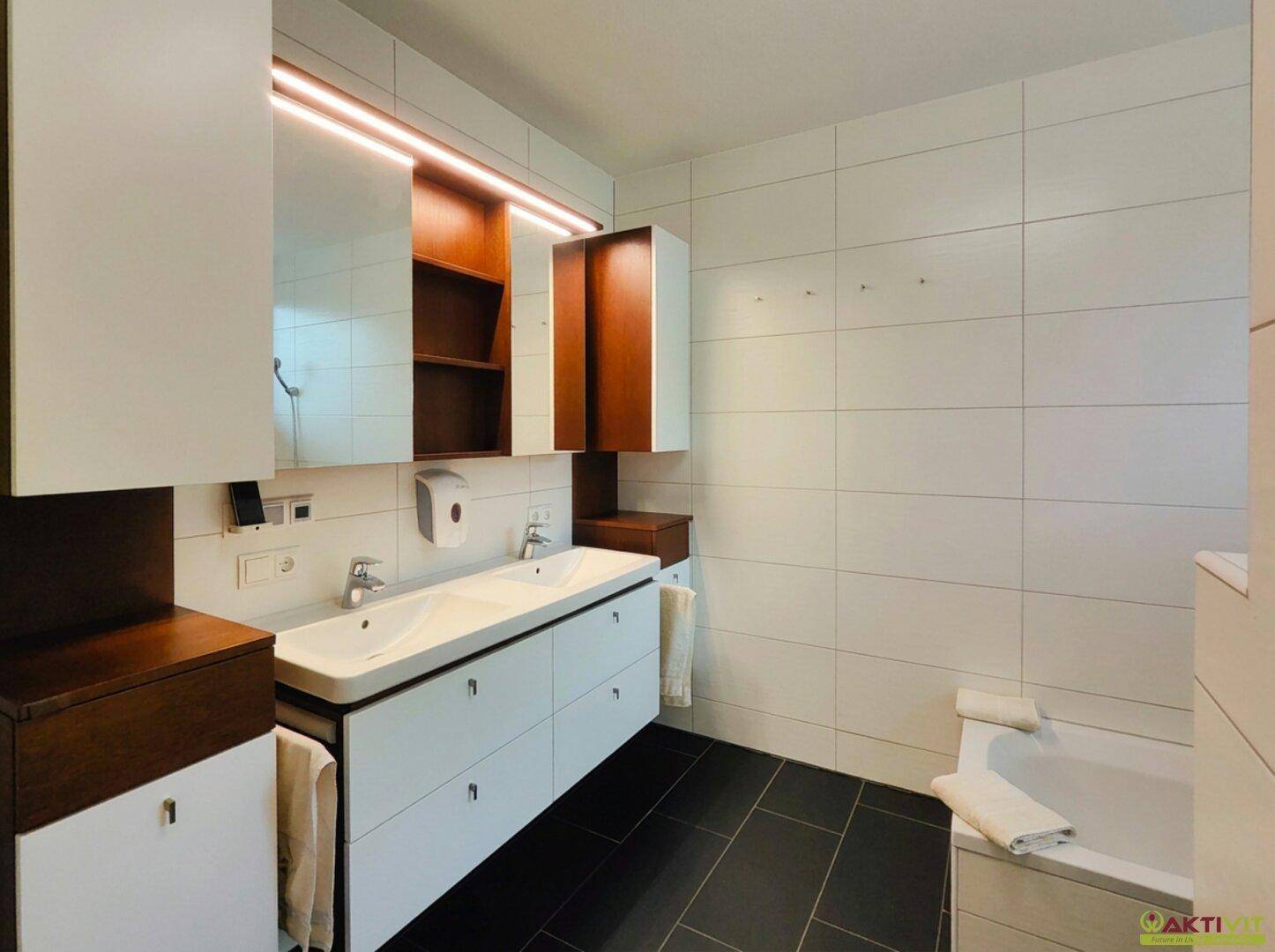 Modernes Badezimmer mit Doppelwaschbecken, weißen Fliesen und dunklem Boden.