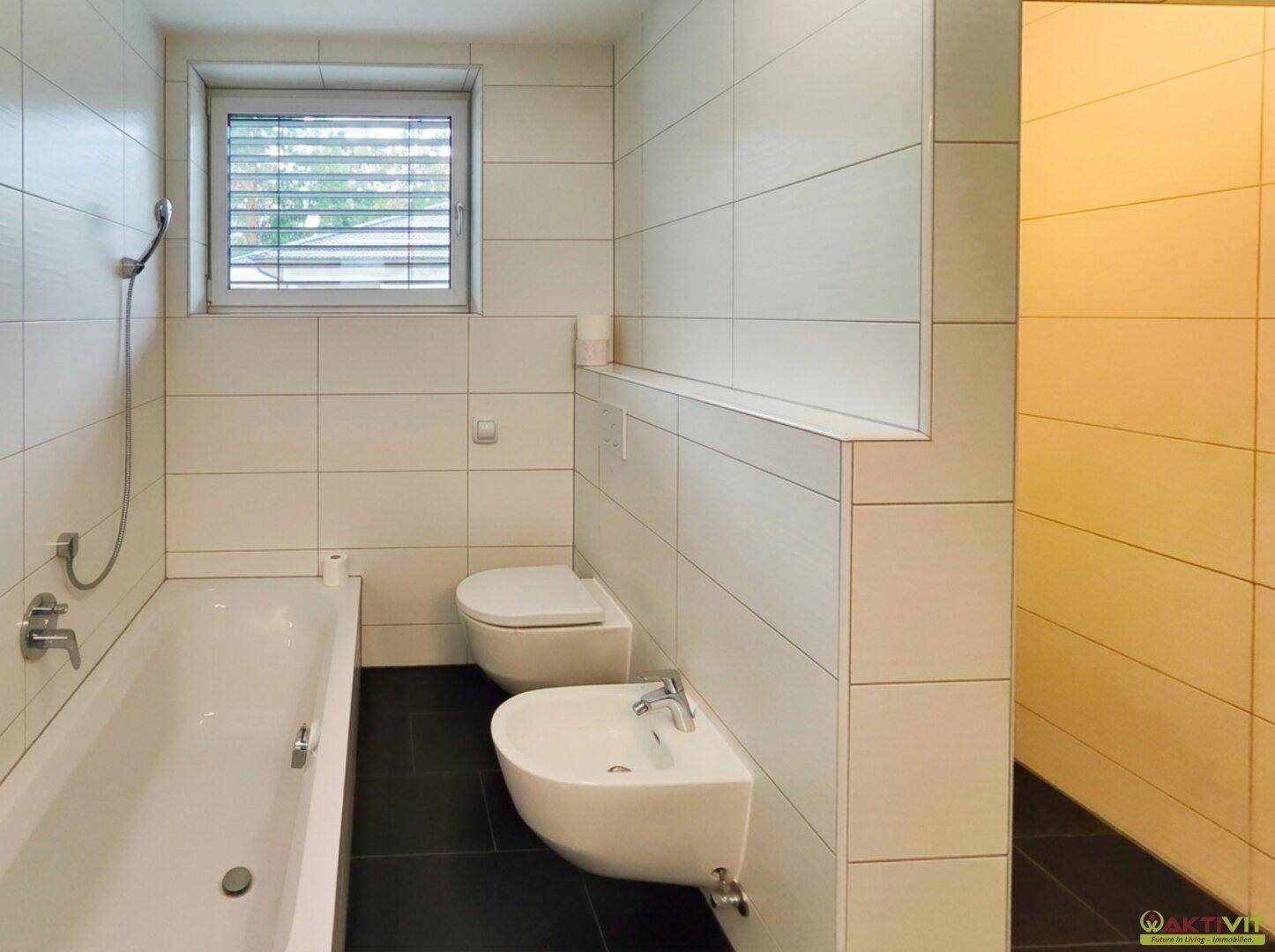 Helles Badezimmer mit Badewanne, Toilette, Bidet und Fenster für natürliche Belüftung.