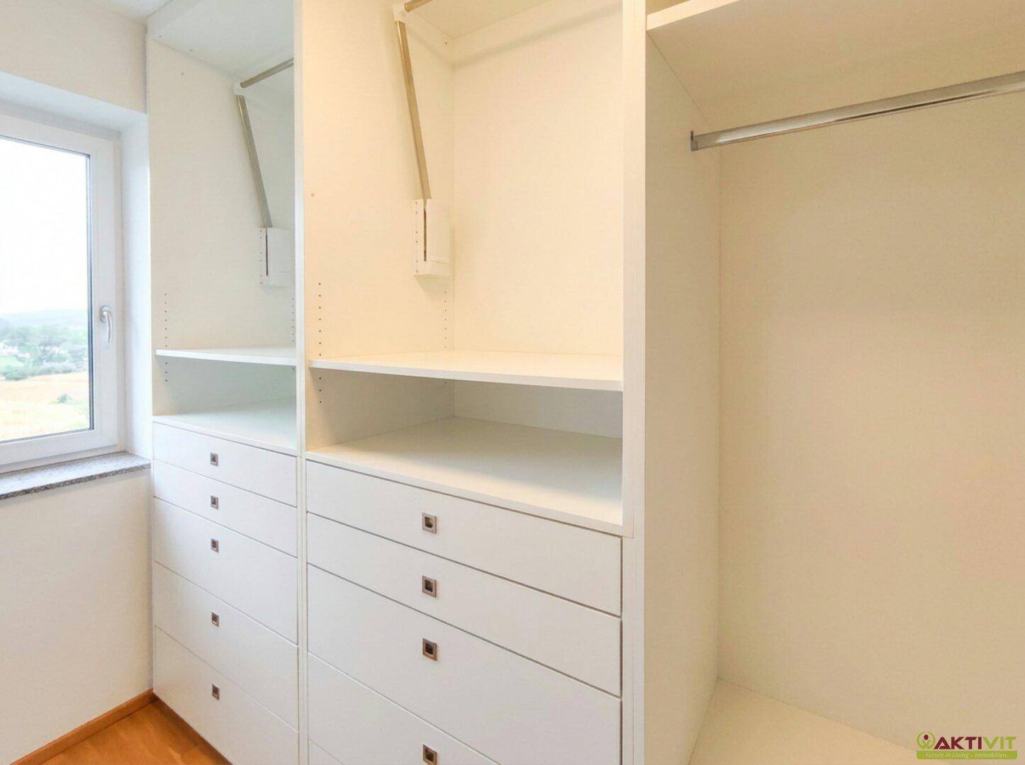 Heller begehbarer Kleiderschrank mit integrierten Regalen und Schubladen sowie Fenster.