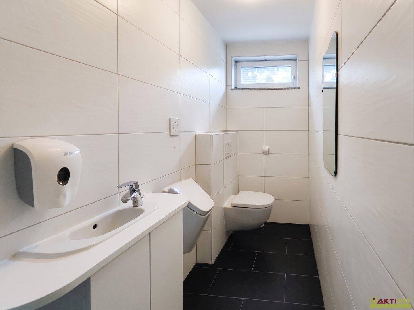 Modernes Gäste-WC mit wandhängender Toilette, Urinal und kleinem Waschbecken.