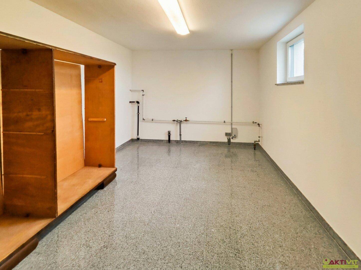 Geräumiger Hauswirtschaftsraum mit sichtbaren Installationen und robustem Boden.