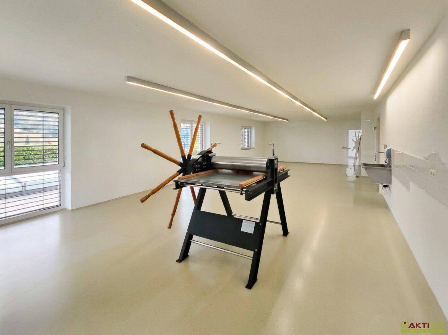 Großer, heller Raum mit Spezialmaschine und Fenstern, vielseitig nutzbar als Werkstatt oder Atelier.