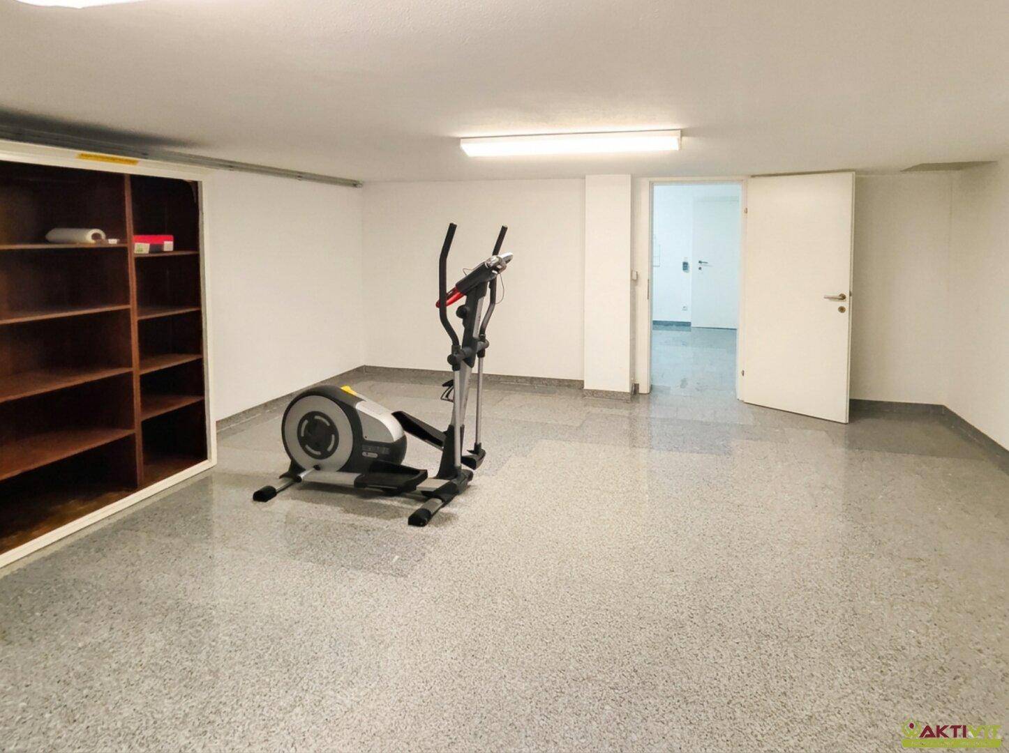 Fitnessraum im Keller mit Trainingsgerät und Regalen für Sportzubehör.