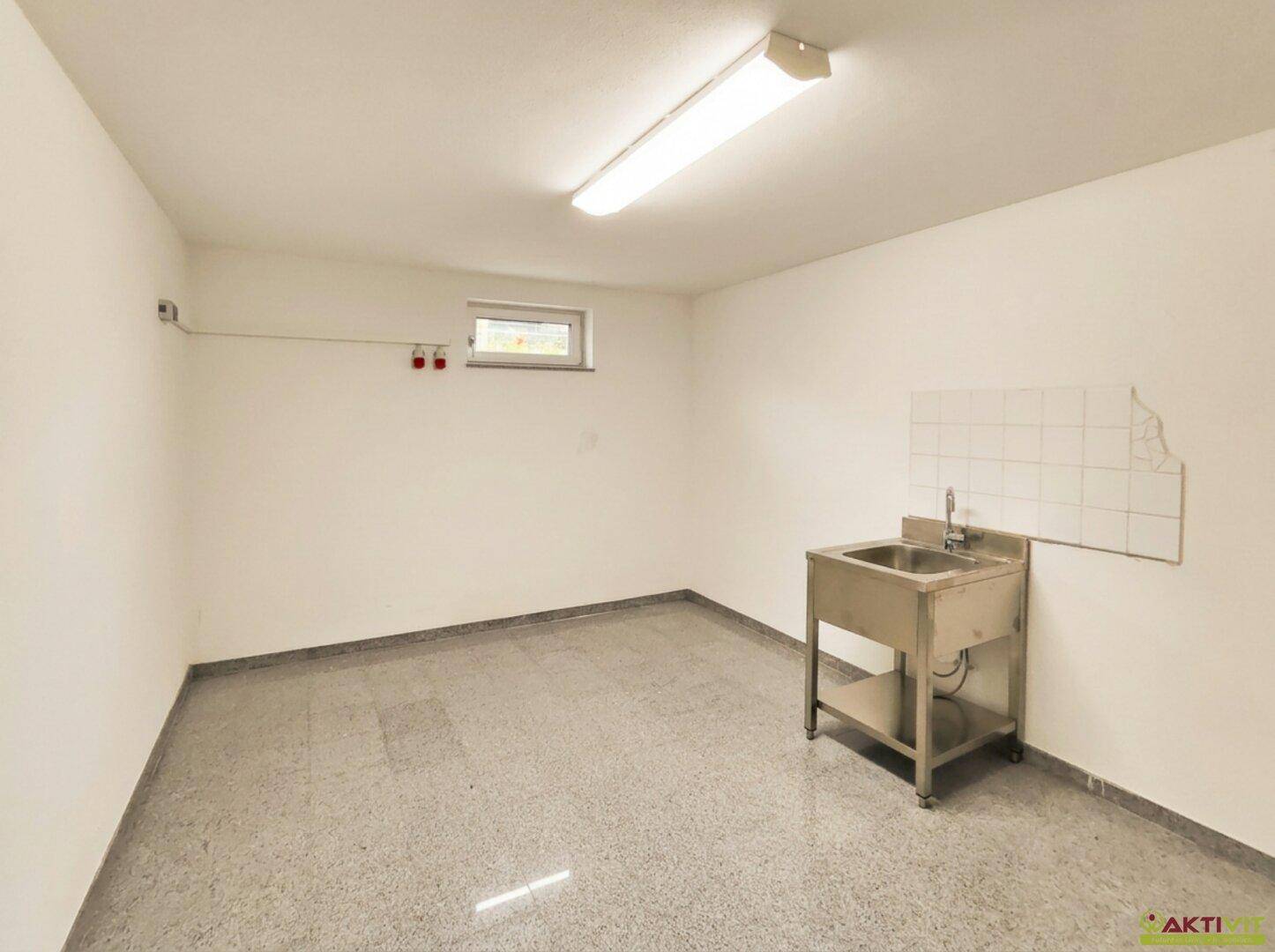 Heller Hauswirtschaftsraum mit gefliestem Boden, kleinem Fenster und Edelstahlspüle.