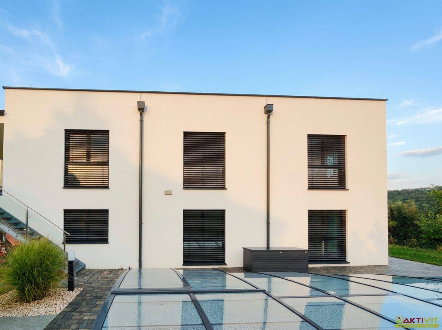 Moderne weiße Hausfassade mit dunklen Fensterläden und einem überdachten Poolbereich.