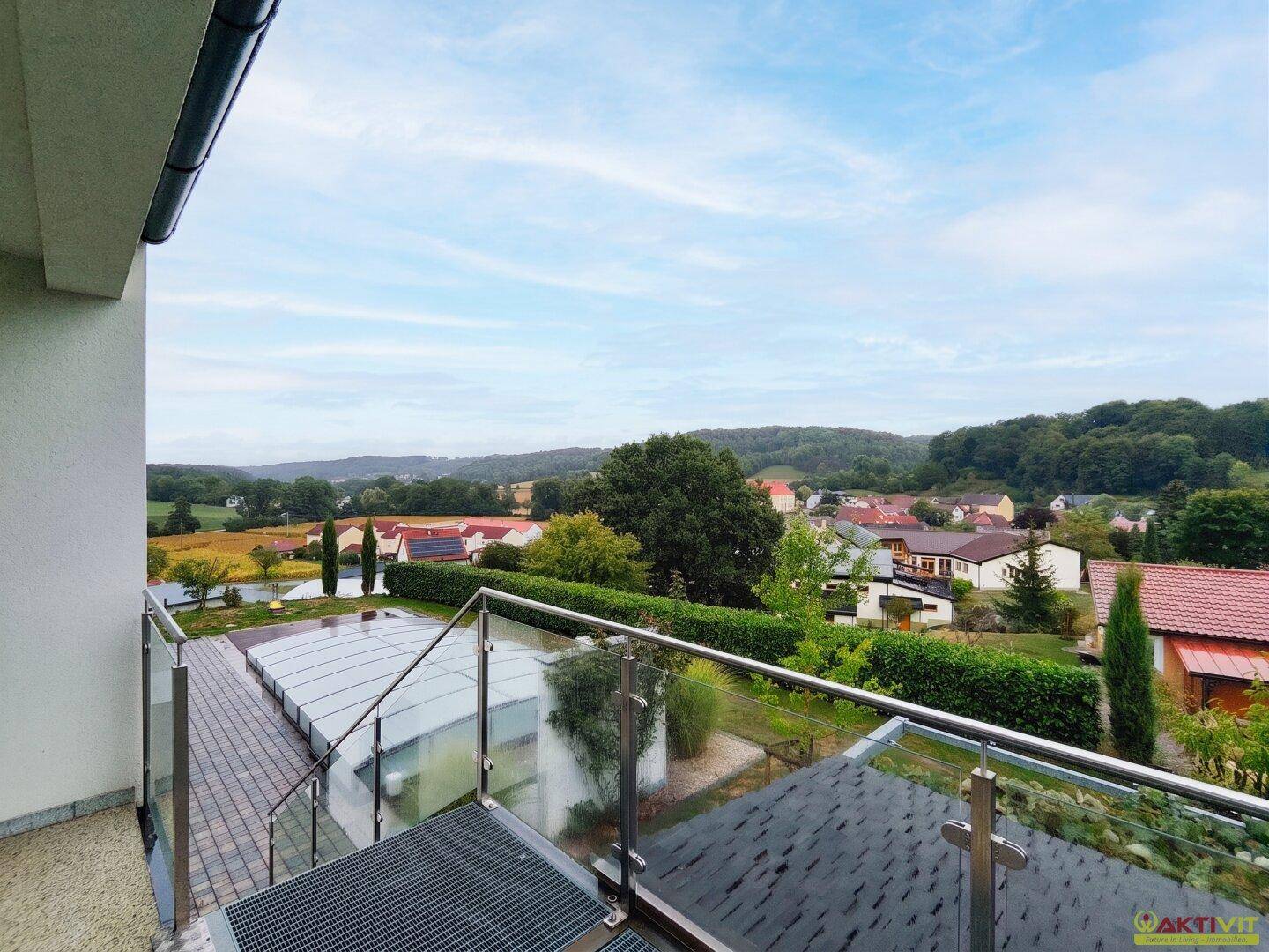 Panoramablick von einem Balkon mit Glasgeländer über die Landschaft und ein Dorf.