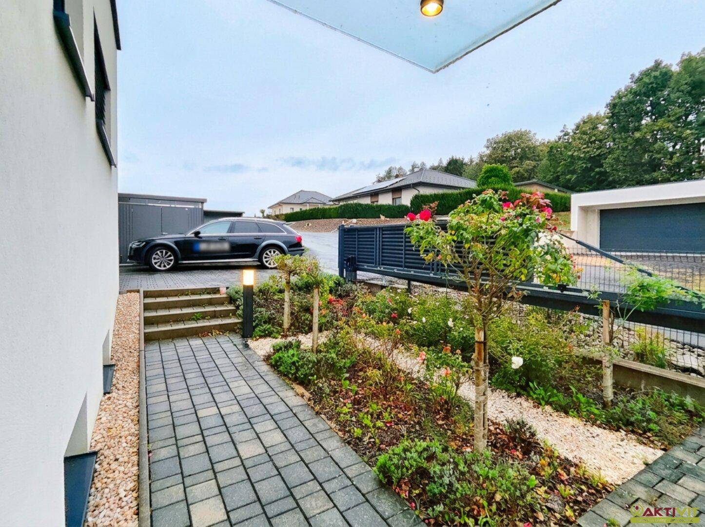 Eingangsbereich des Hauses mit gepflastertem Weg, bepflanzten Beeten und einer Einfahrt.