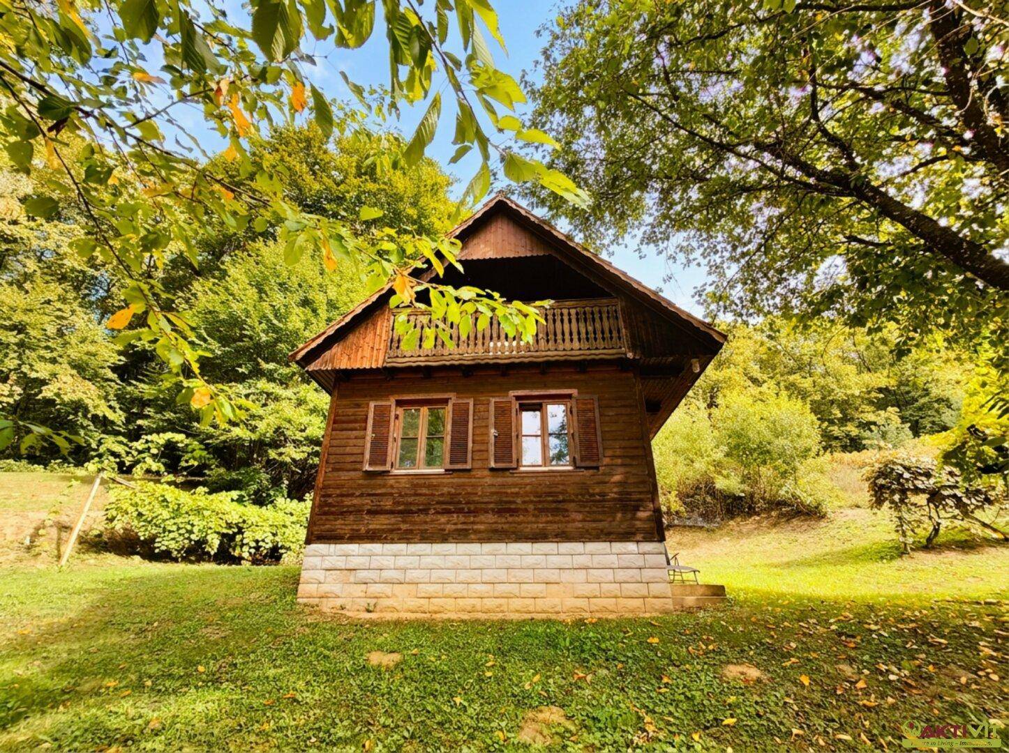 Charmantes Holzhaus mit kleinem Balkon, umgeben von üppiger grüner Natur und Bäumen.