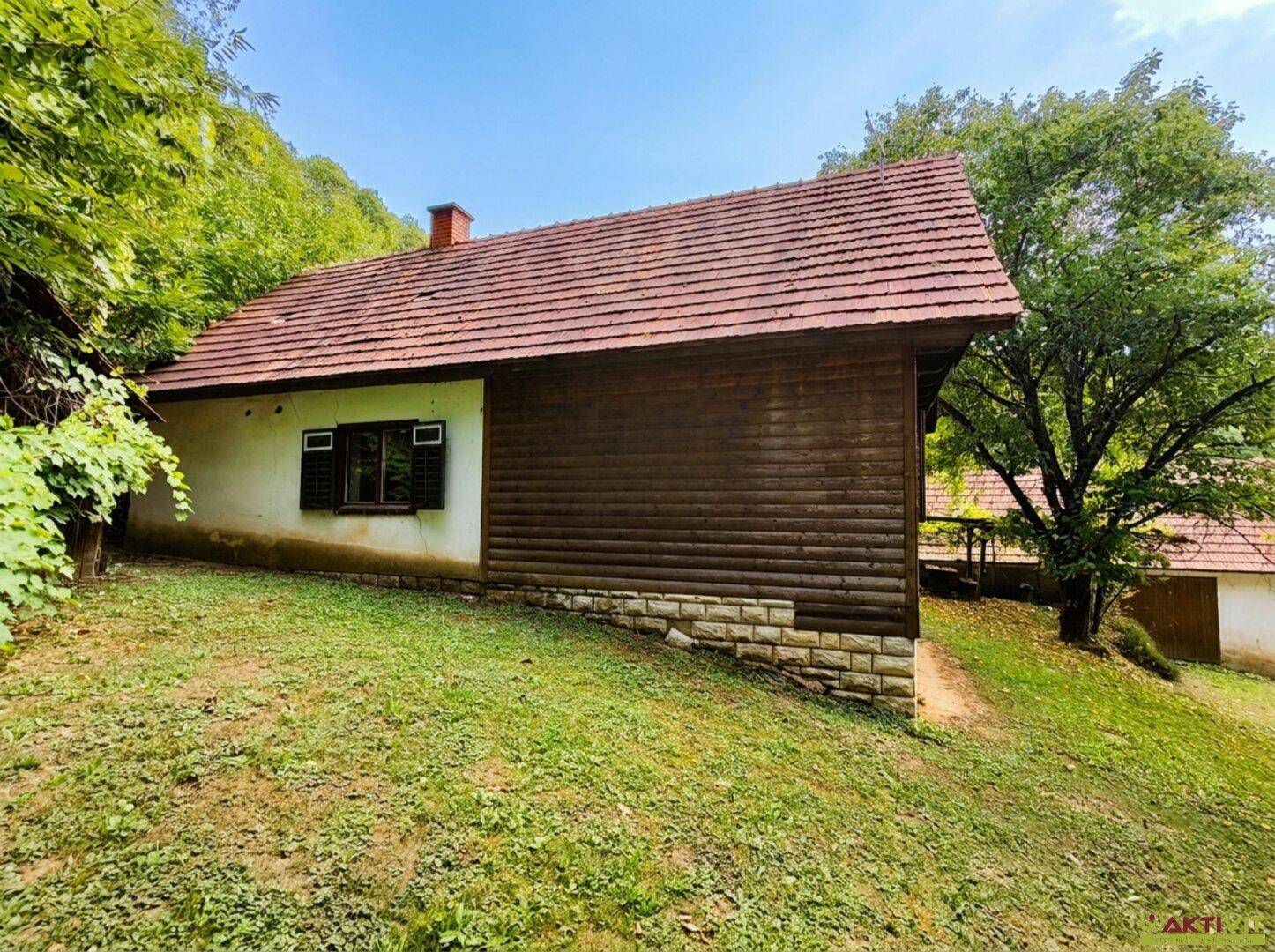 Ländliches Haus mit weiß getünchter Fassade und Holzelementen, umgeben von grünen Hügeln.
