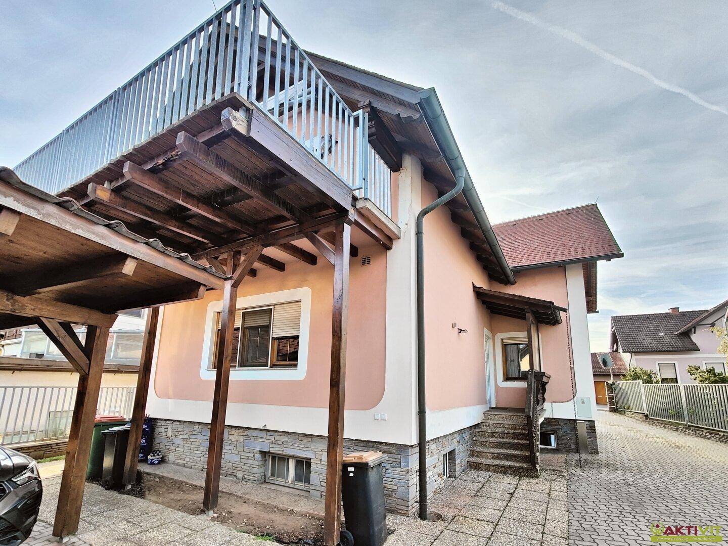 Seitenansicht des Hauses mit überdachtem Carport und einem großen Balkon im oberen Stockwerk.