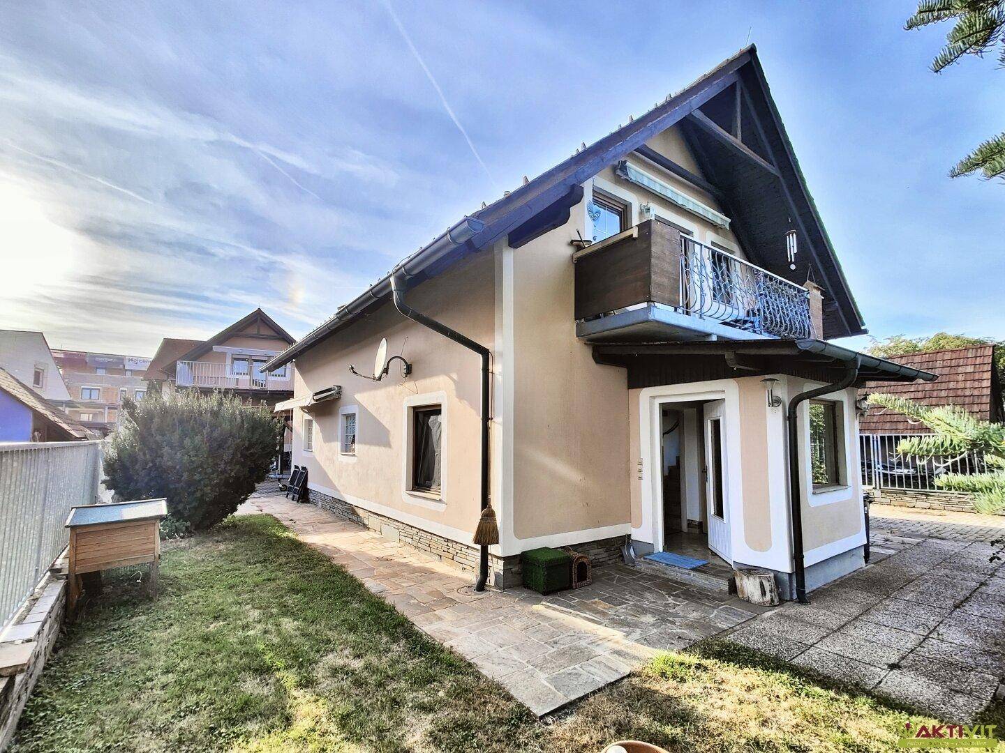 Seitenansicht des Hauses mit Zugang zum Garten und einer kleinen gepflasterten Fläche.