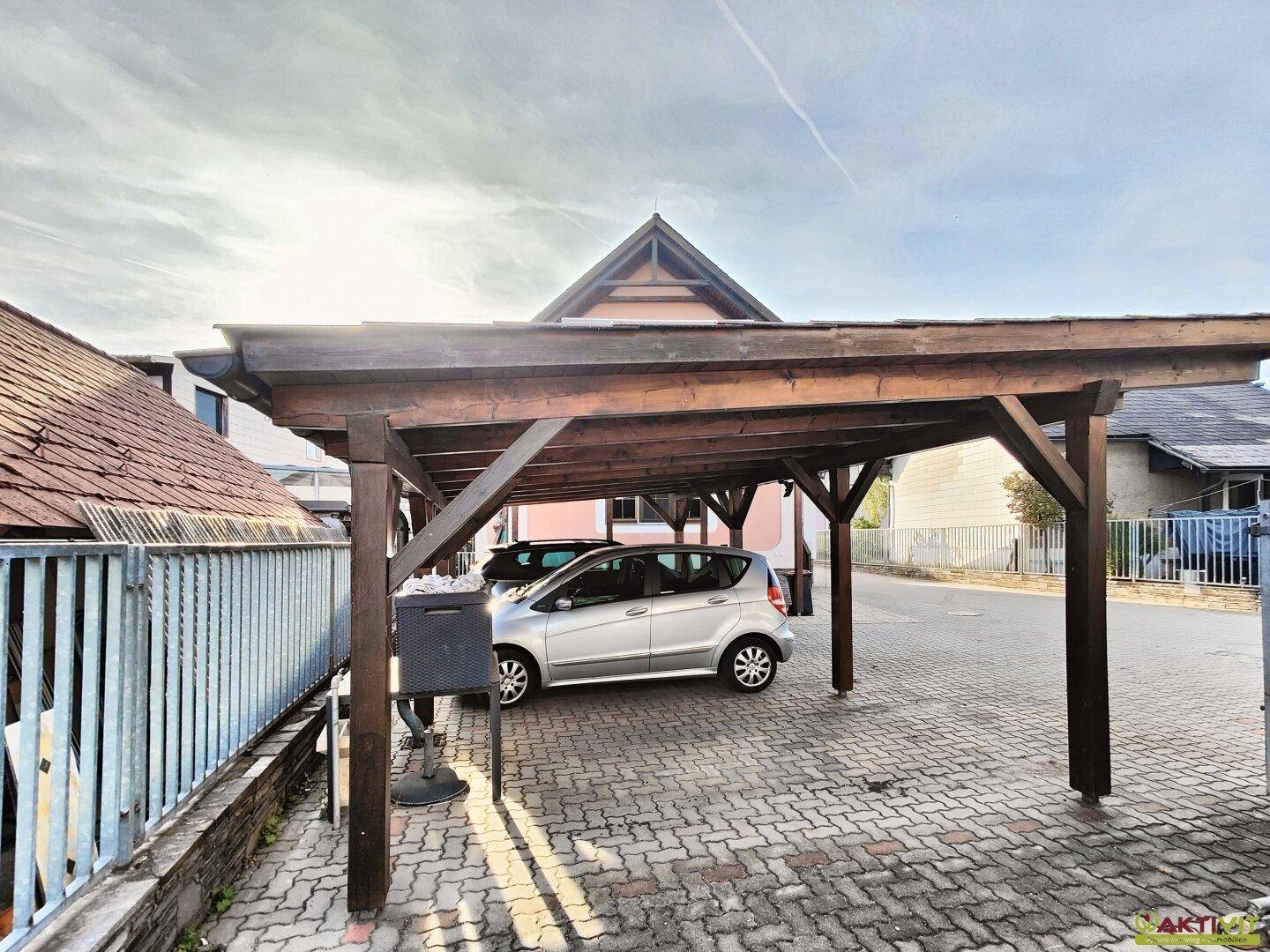 Überdachter Carport aus Holz bietet Schutz für Fahrzeuge vor Witterungseinflüssen.