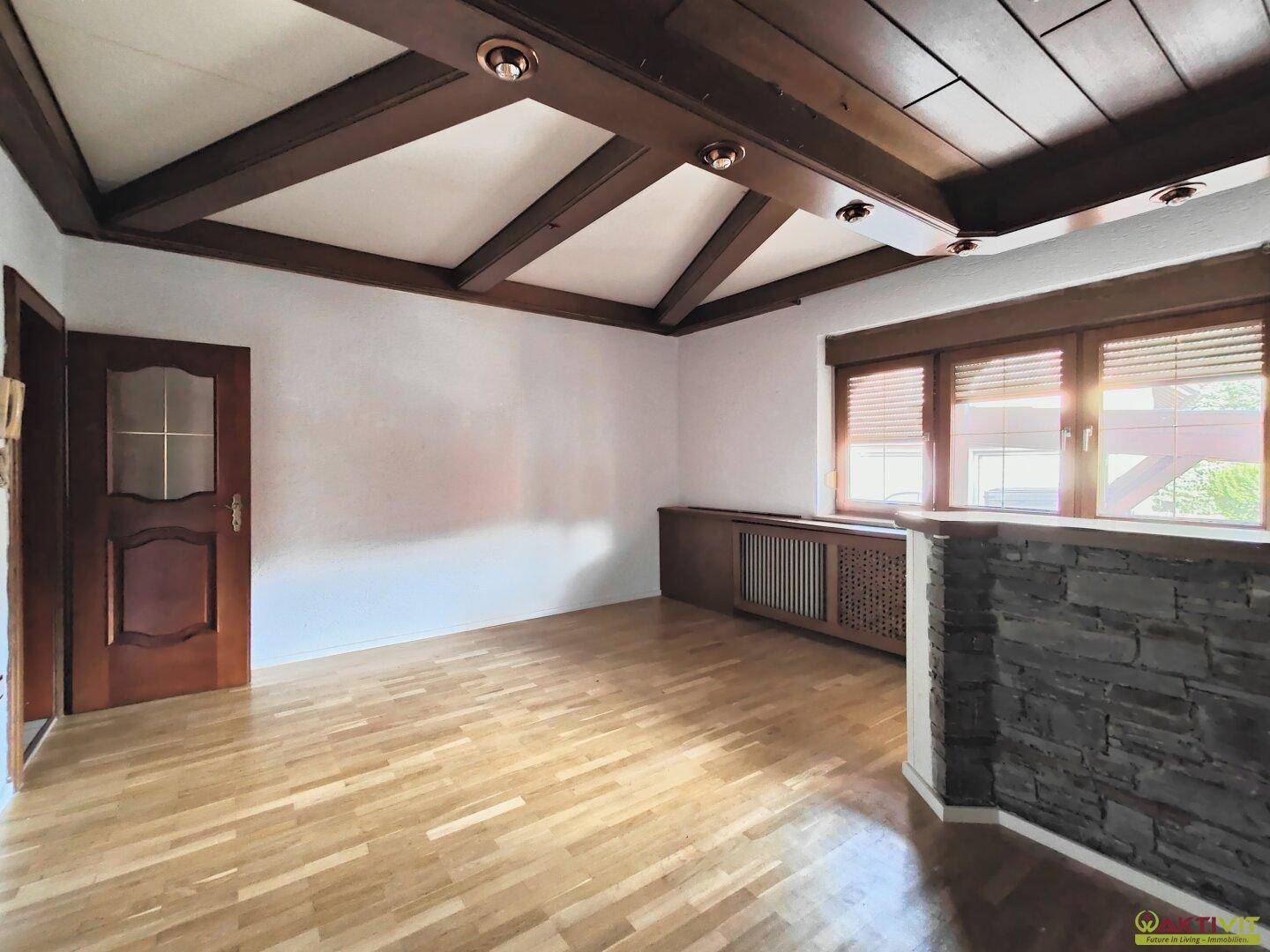 Helles Wohnzimmer mit sichtbaren Holzbalken, Parkettboden und einer rustikalen Steinwand.