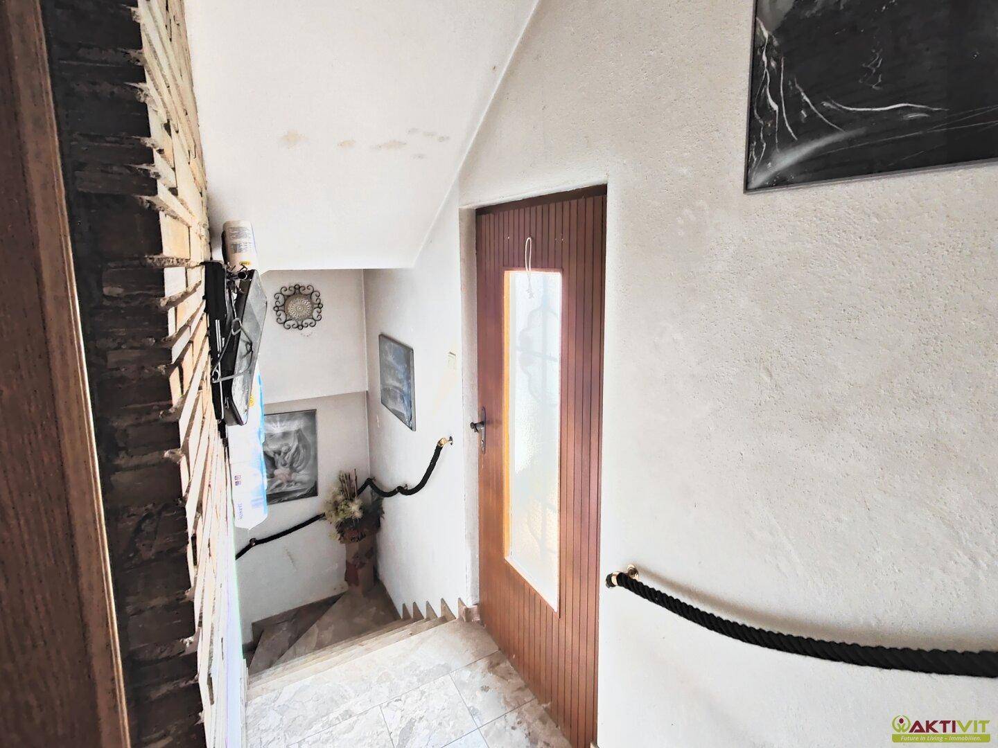 Treppenhaus mit rustikaler Steinwand und Seilgeländer, das zu den oberen Stockwerken führt.