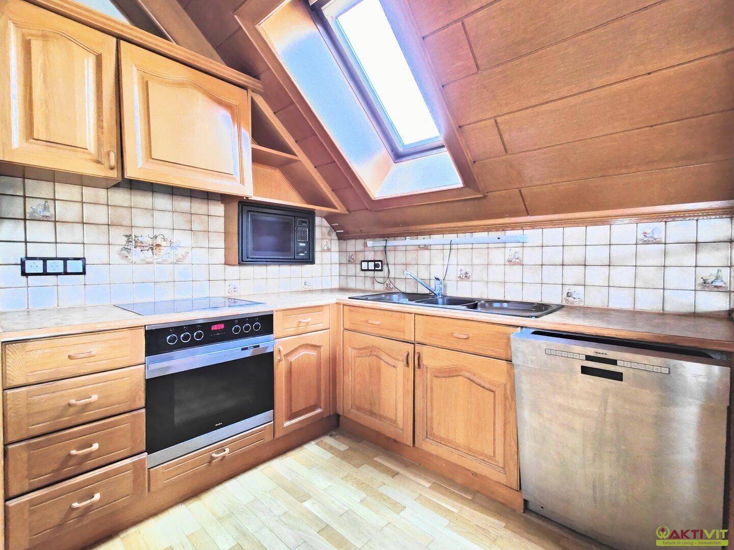 Funktionale Küche im Dachgeschoss mit Holzschränken, Fliesenrückwand und Dachfenster.