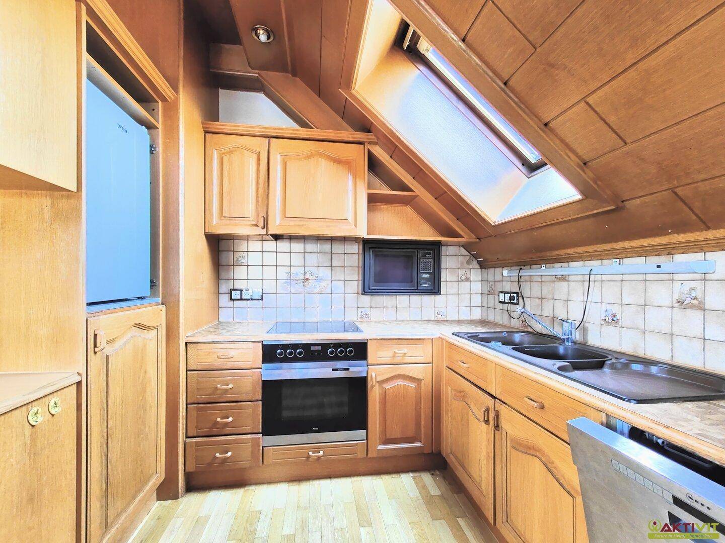 Helle Dachgeschossküche mit Holzfronten, modernen Geräten und einem praktischen Dachfenster.
