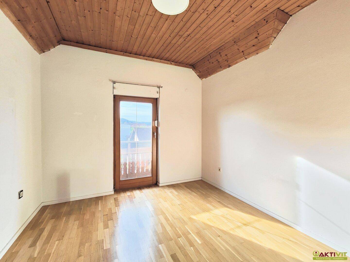 Schlafzimmer mit Holzboden, weiß gestrichenen Wänden und Zugang zu einem Balkon.
