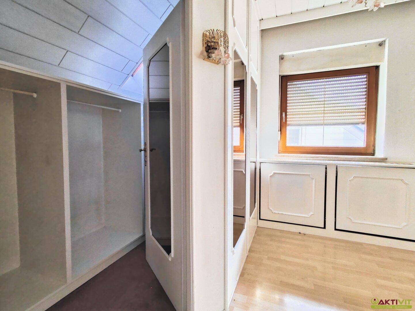 Begehbarer Kleiderschrank mit Regalen und Spiegeltüren in einem Dachzimmer.