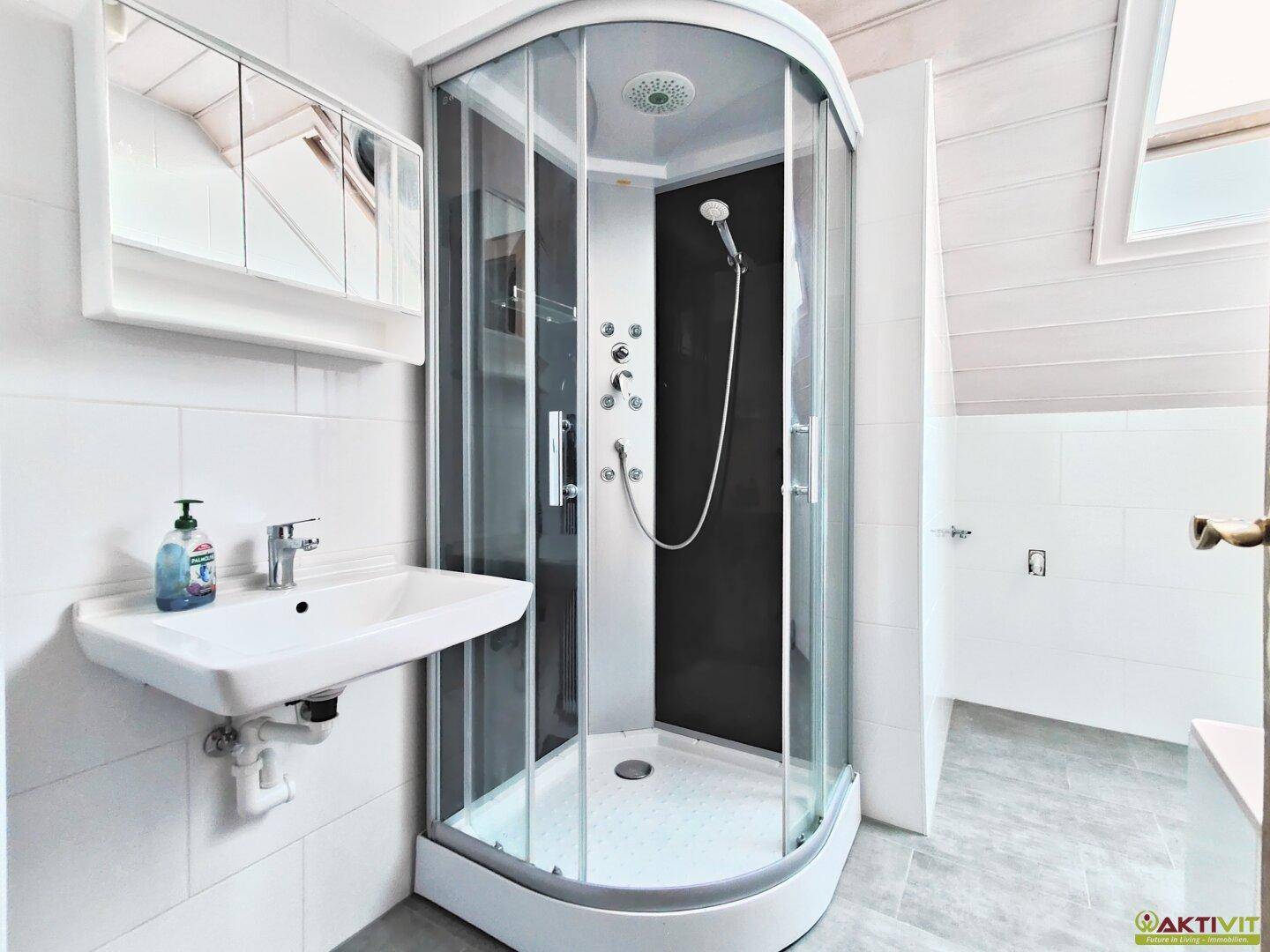Modernisierte Dusche mit Glasabtrennung, Waschbecken und Spiegelschrank im Dachgeschoss.