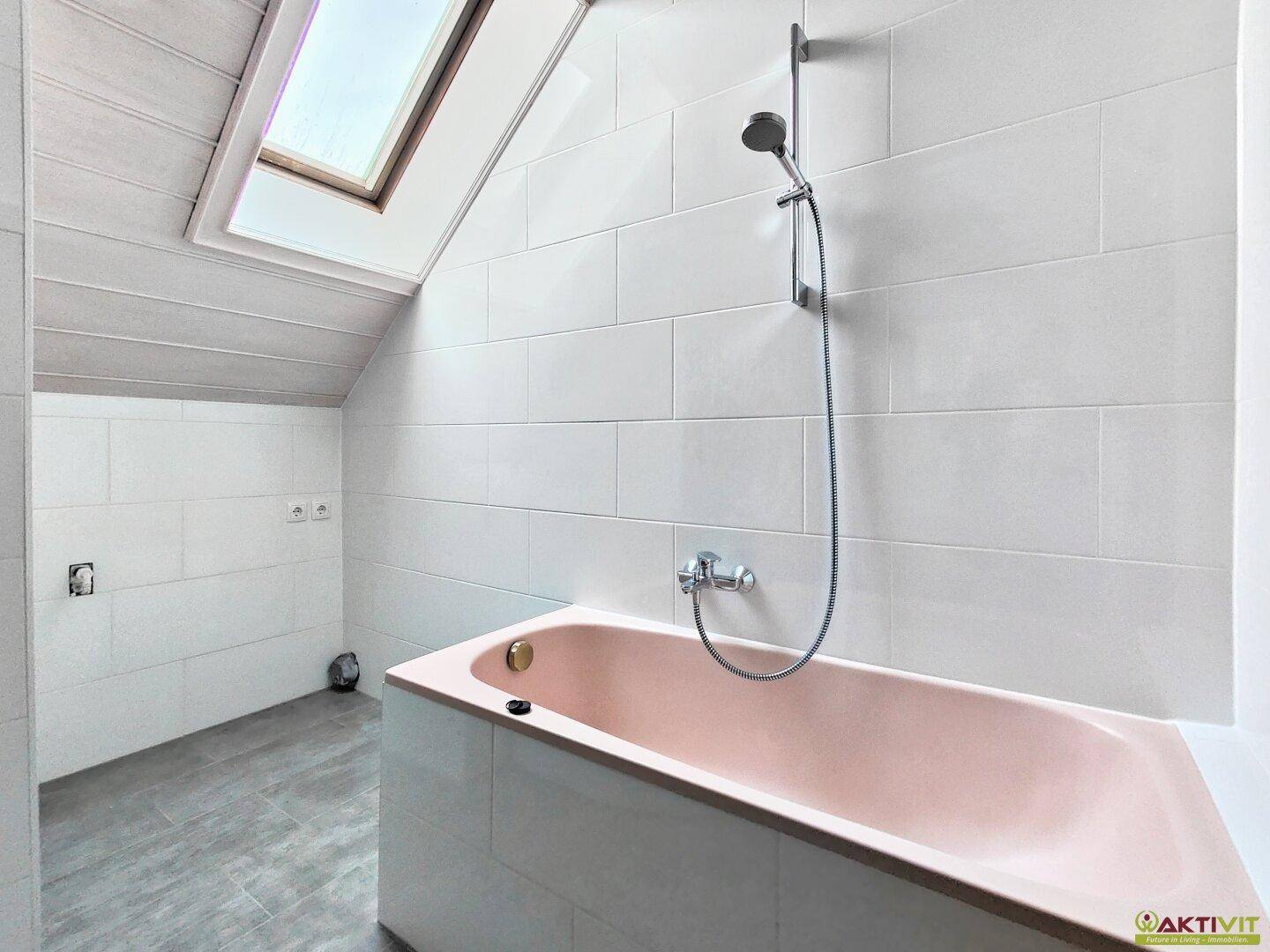 Badezimmer mit rosa Badewanne, weißen Fliesen und Dachfenster, bereit zur Fertigstellung.