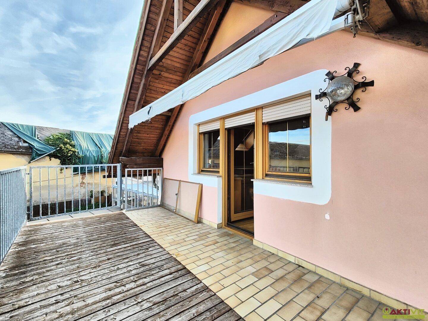 Dachterrasse mit Holzboden, Markise und Zugang zum Innenbereich, umgeben von ländlicher Idylle.