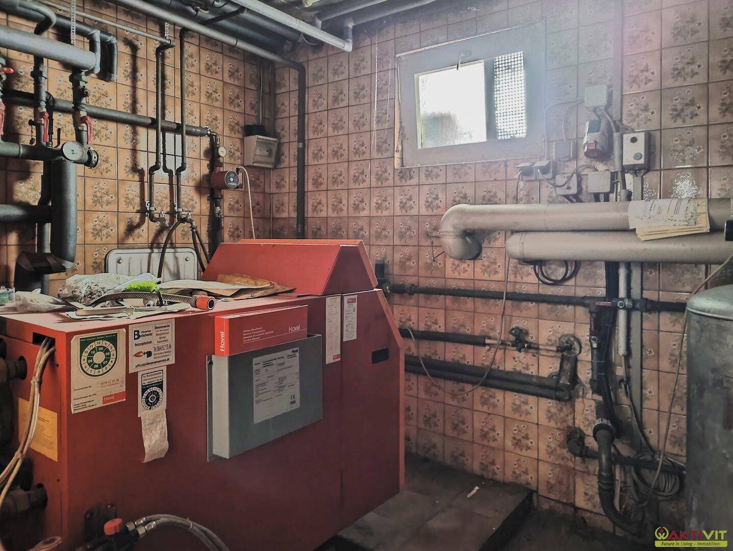 Heizungsraum mit Kessel, Rohren und gefliesten Wänden, zeigt die technische Ausstattung des Hauses.