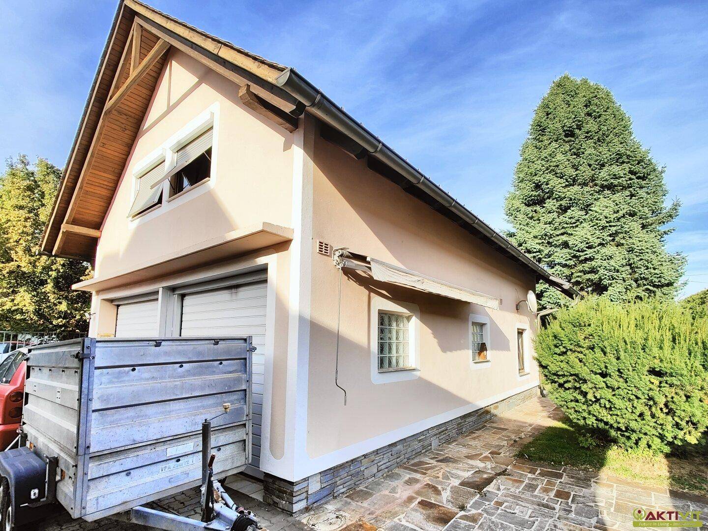 Separate Garage mit Satteldach und einem Anhänger davor, umgeben von Grün.