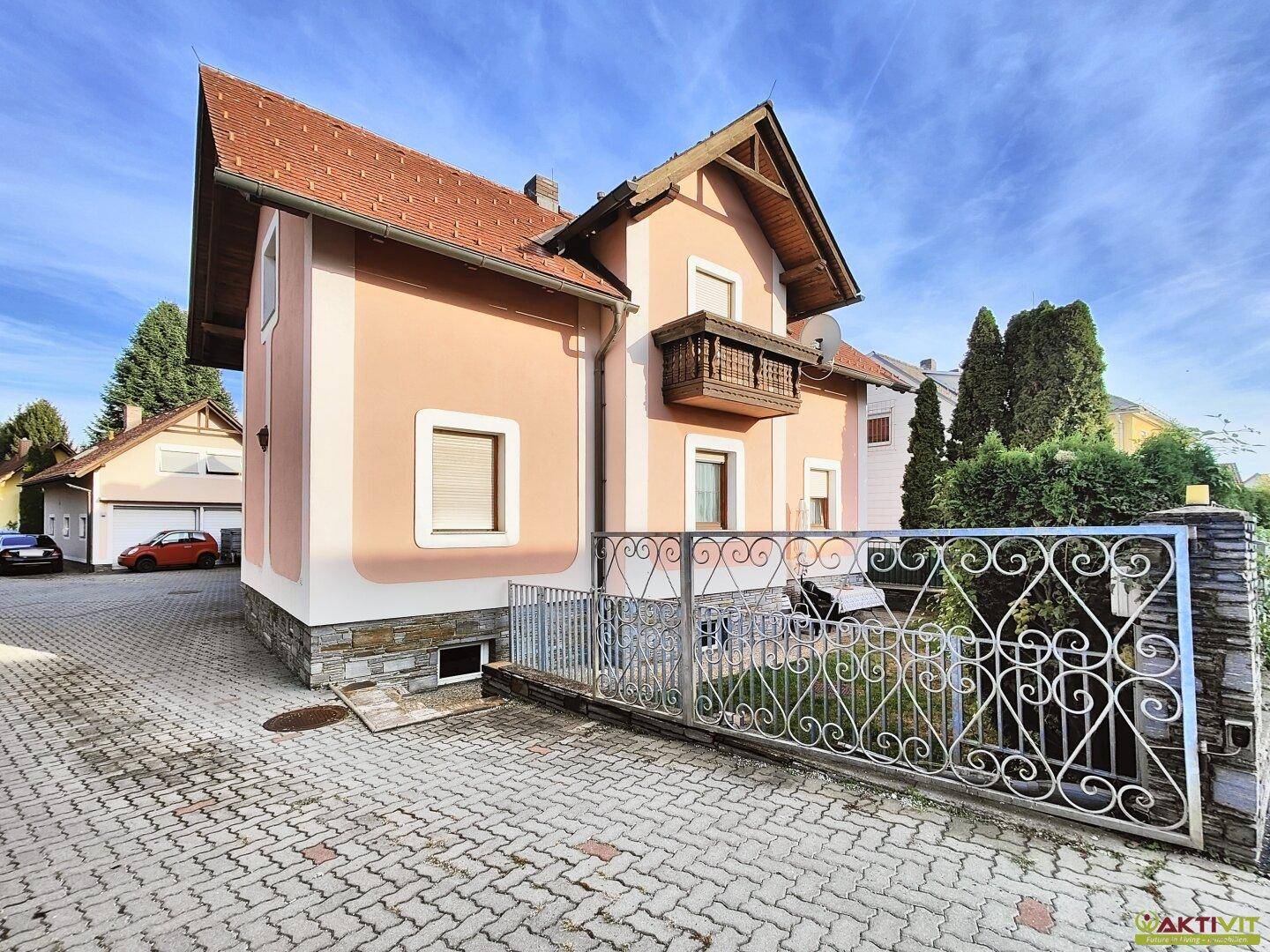 Ansicht des Hauses von der Einfahrt mit dekorativem Zaun und gepflastertem Bereich.