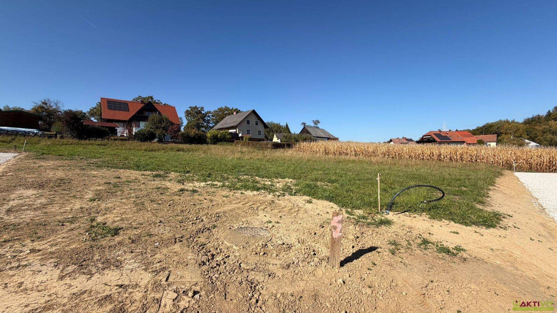Blick über ein unbebautes Grundstück mit Erdboden und Gras, umgeben von ländlicher Bebauung.