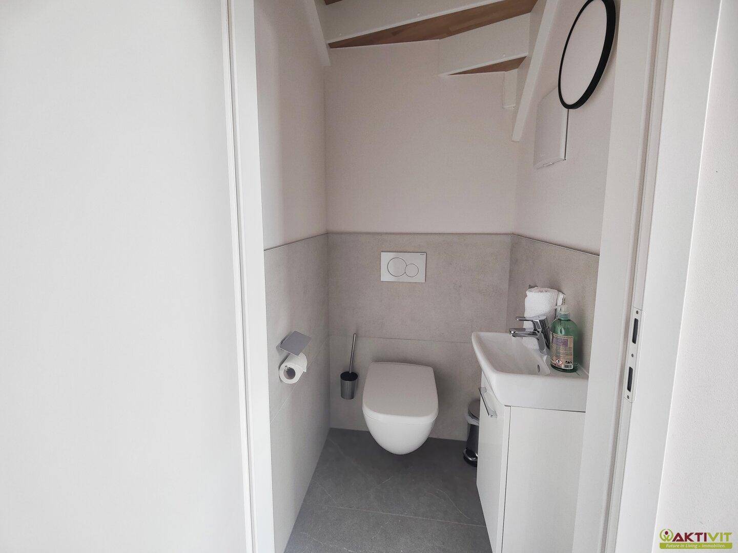 Kleines, modernes Gäste-WC mit Wand-WC, Waschbecken und grauen Fliesen.