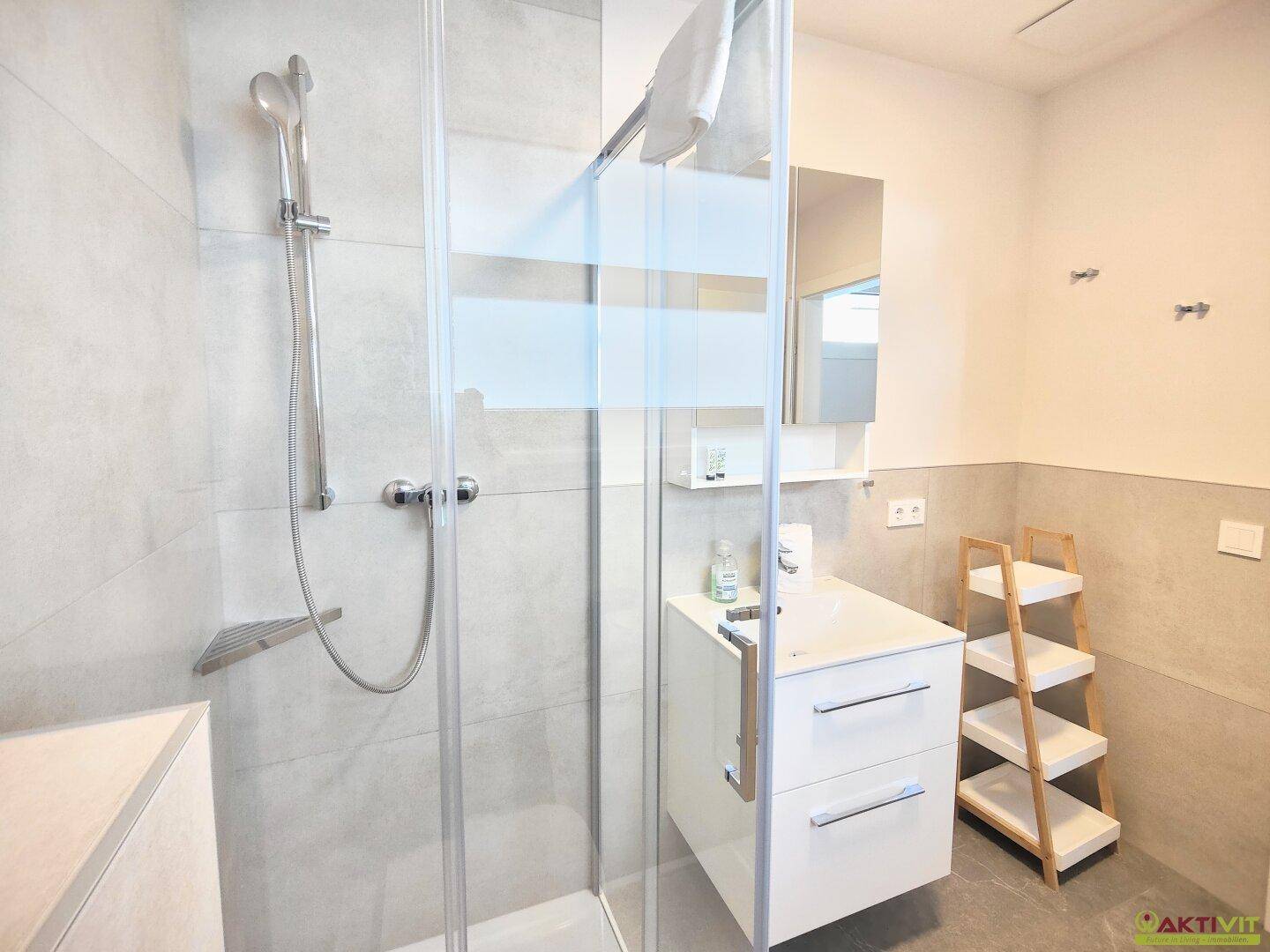 Modernes Badezimmer mit Duschkabine, Waschbecken und Spiegelschrank, hell gefliest.