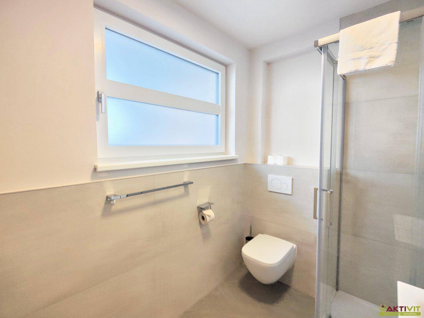 Helles Badezimmer mit Dusche, WC und Fenster, ausgestattet mit modernen Armaturen.