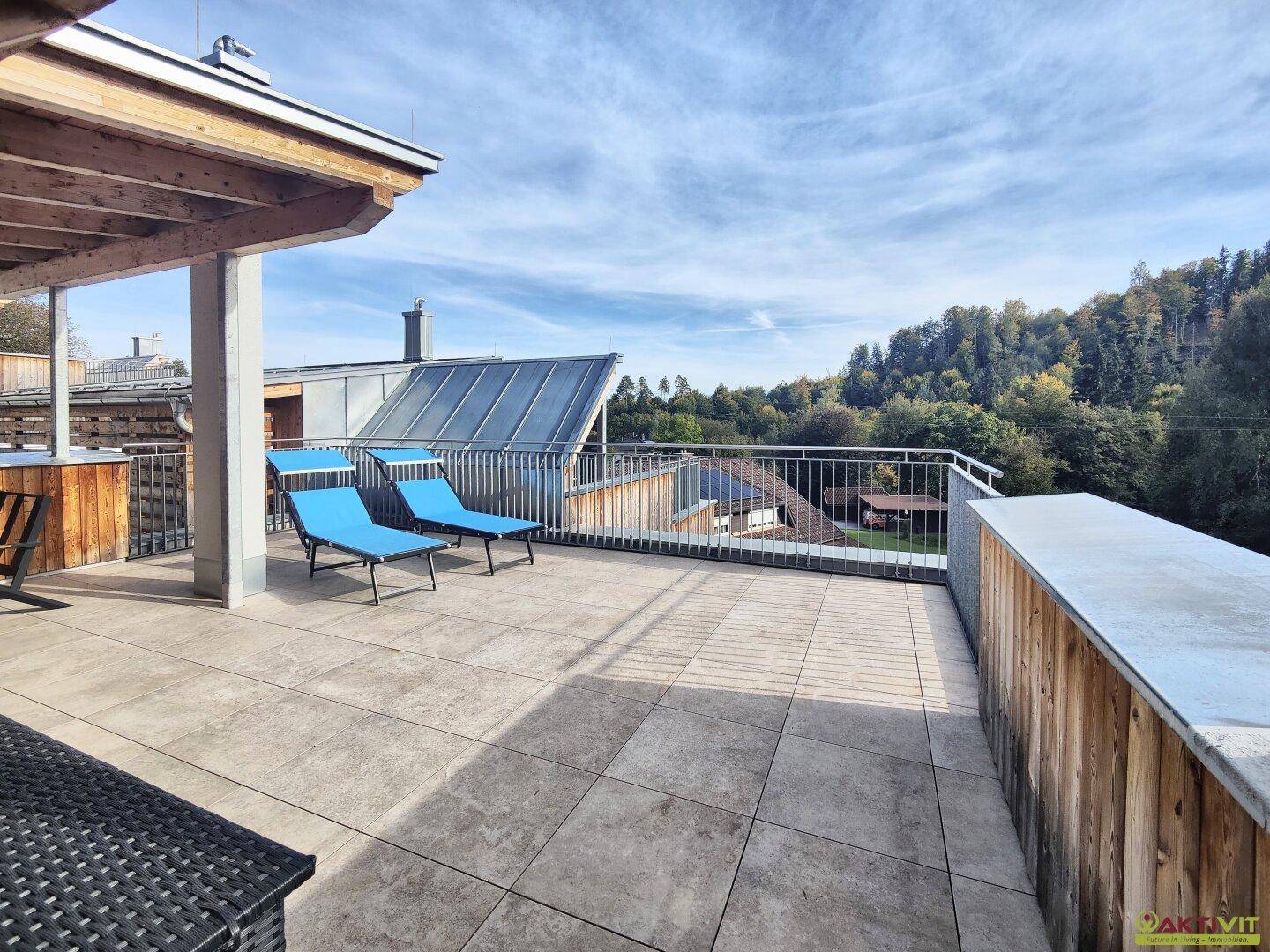 Geräumige Dachterrasse mit weitem Blick auf die grüne Umgebung und die umliegenden Häuser.