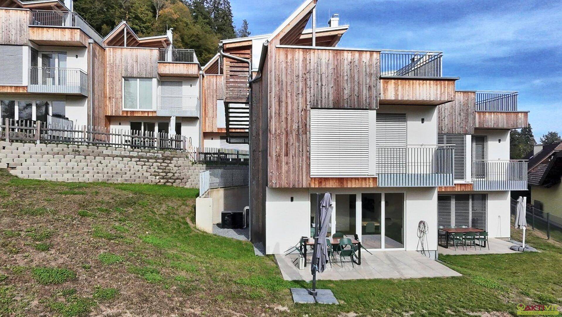Moderne Wohnanlage mit Holzfassaden und Terrassen, eingebettet in eine grüne Hügellandschaft.