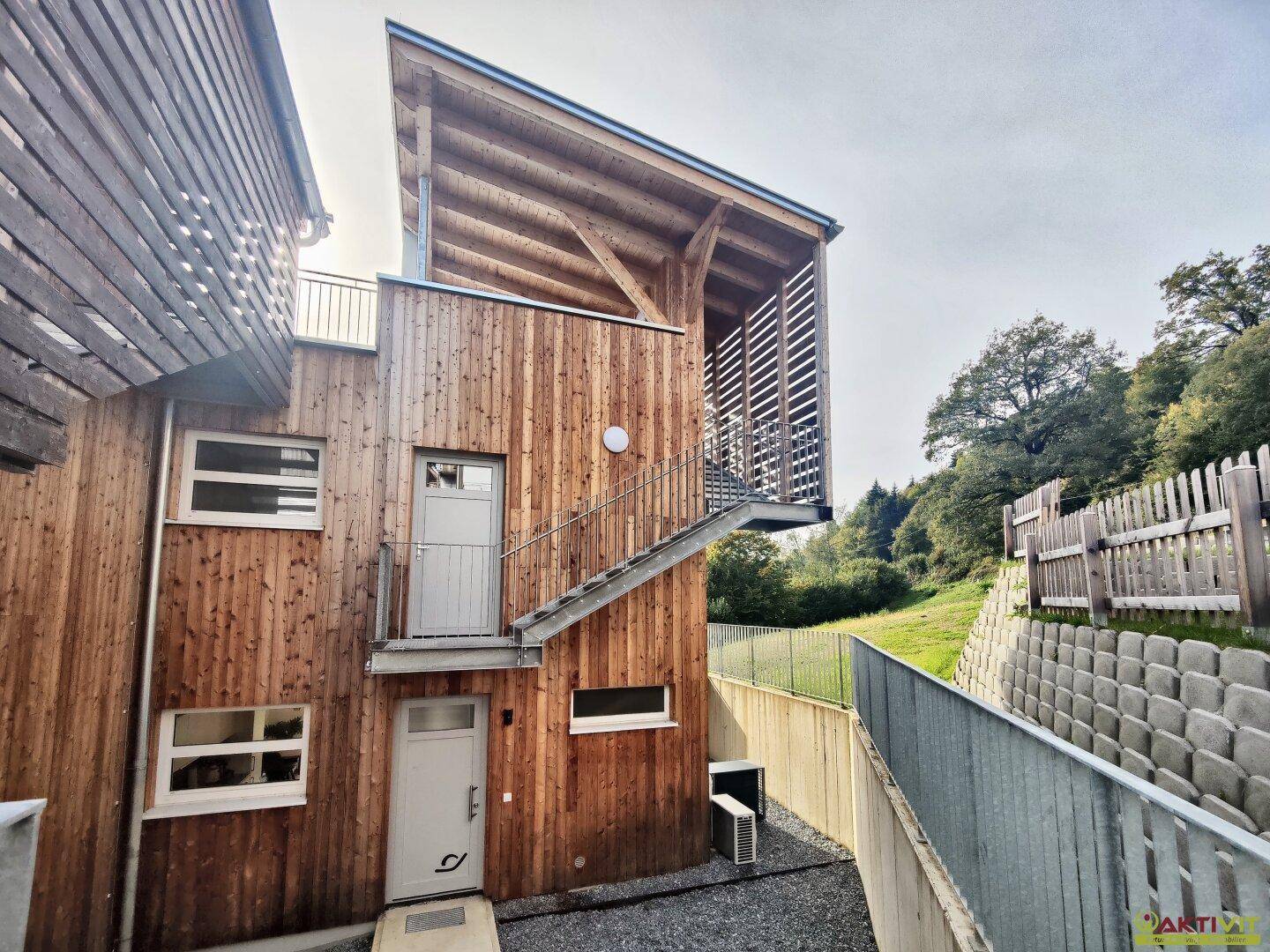 Eingangsbereich eines modernen Gebäudes mit Holzfassade und Außentreppe.