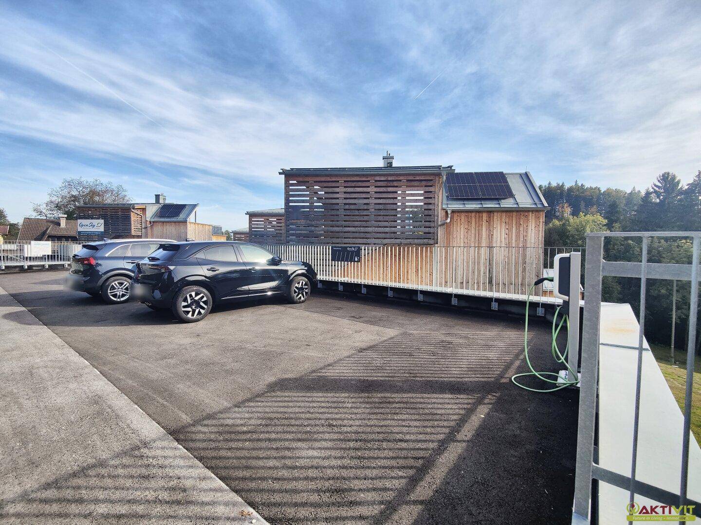 Außenparkplätze mit Ladestation für Elektrofahrzeuge, umgeben von moderner Architektur.