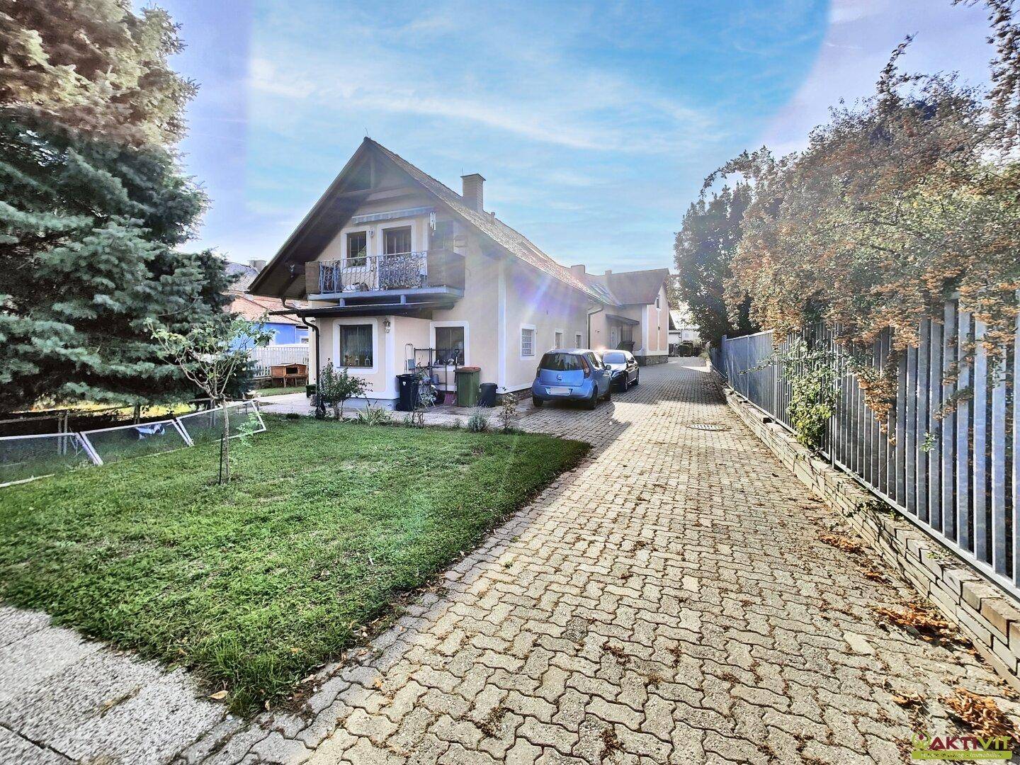 Das Haus von der langen Einfahrt aus gesehen, umgeben von einem grünen Garten.