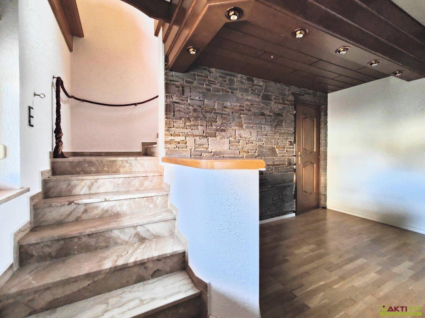 Marmortreppe mit Steinwand und Holzgeländer führt in die oberen Etagen des Hauses.