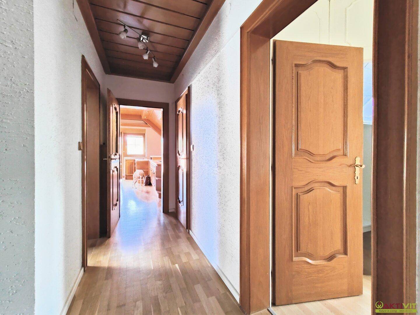 Langer Flur mit Holztüren und Holzdeckenverkleidung, der zu verschiedenen Räumen führt.