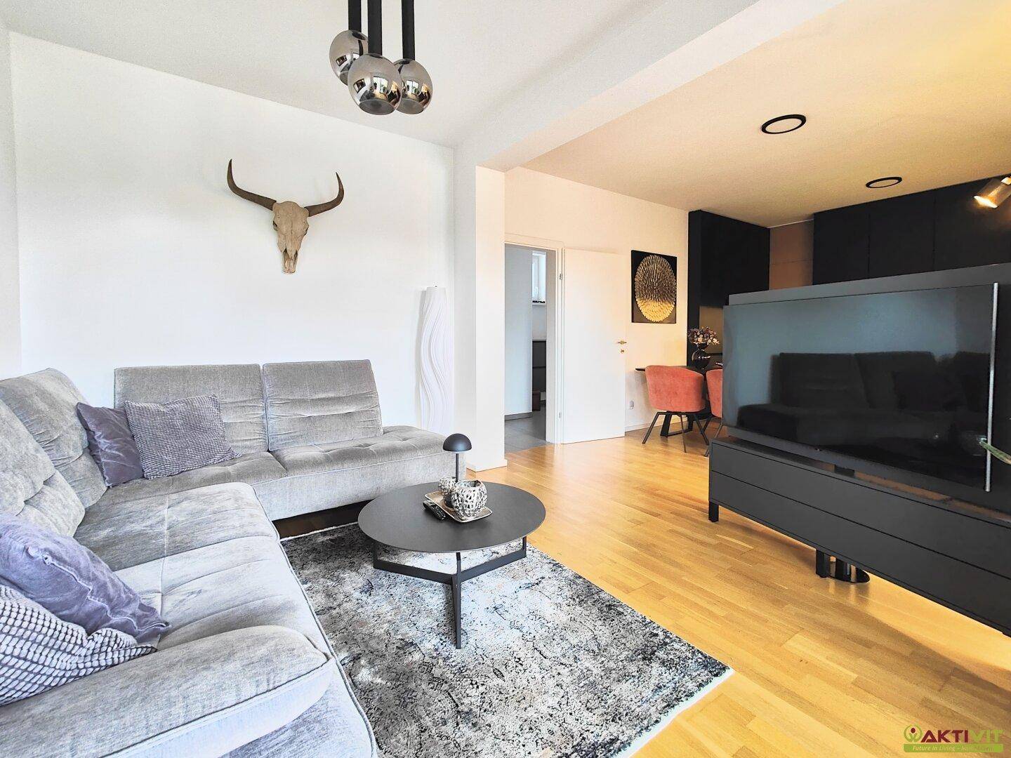 Offener Wohnbereich mit gemütlichem Sofa, Fernseher und Blick auf den Ess- und Küchenbereich.