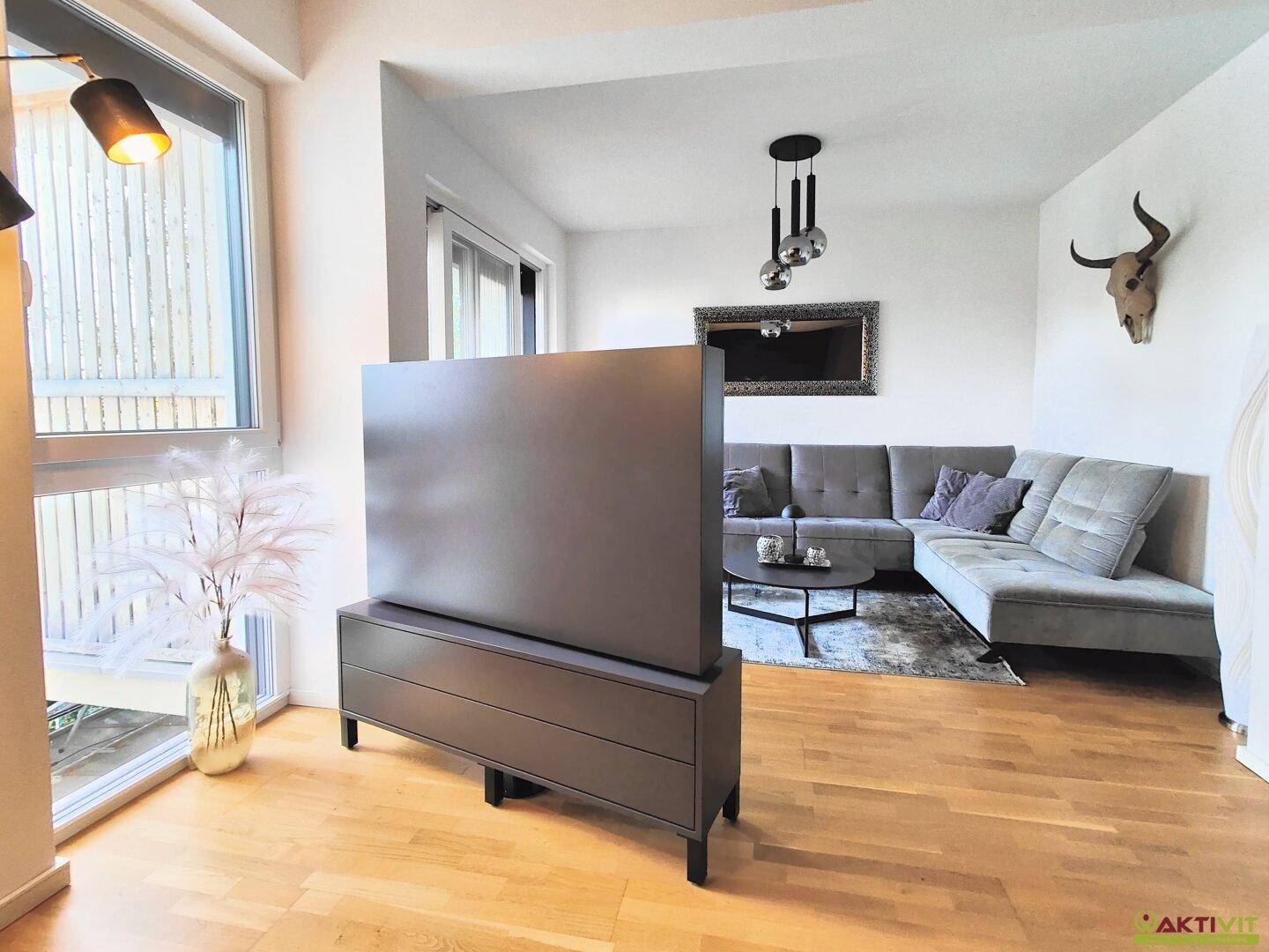 Geräumiges Wohnzimmer mit Holzboden, modernem TV-Möbel und viel Tageslicht.