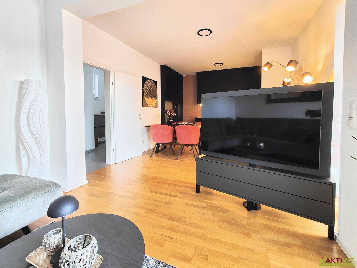 Moderner Wohn- und Essbereich mit Holzboden, großem Fernseher und offener Küche.