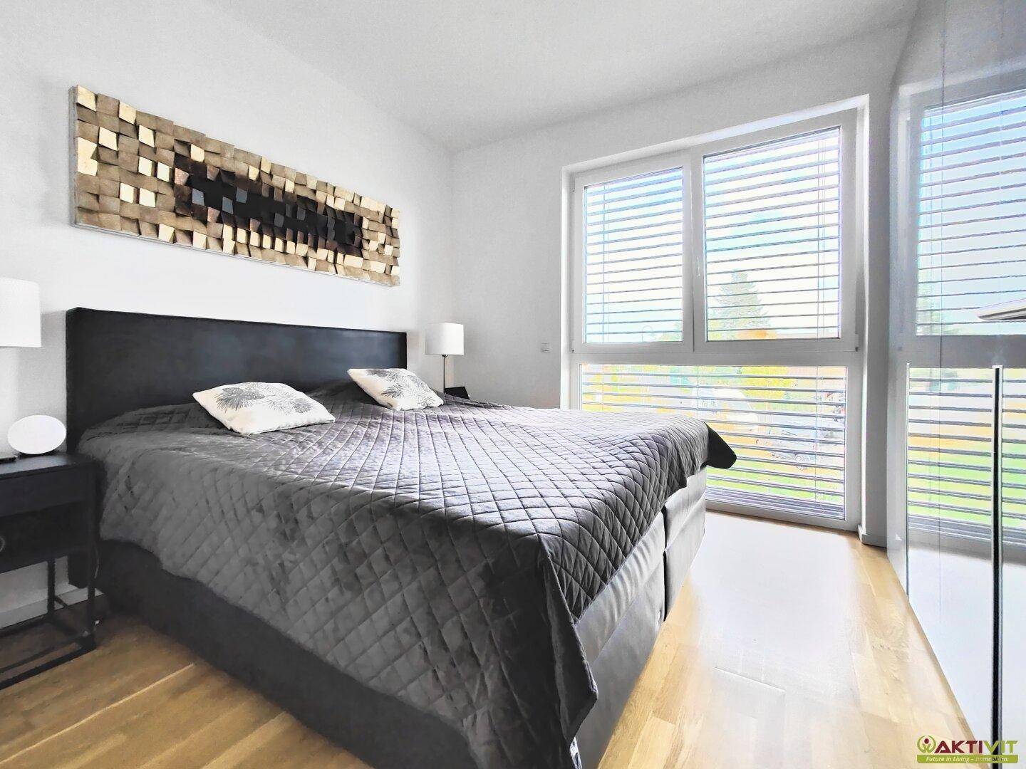 Helles Schlafzimmer mit großem Doppelbett, Holzboden und breitem Fenster mit Jalousien.