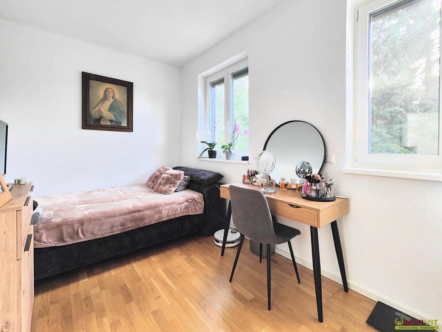 Gemütliches Schlafzimmer mit Einzelbett, Holzboden und einem Schminktisch am Fenster.