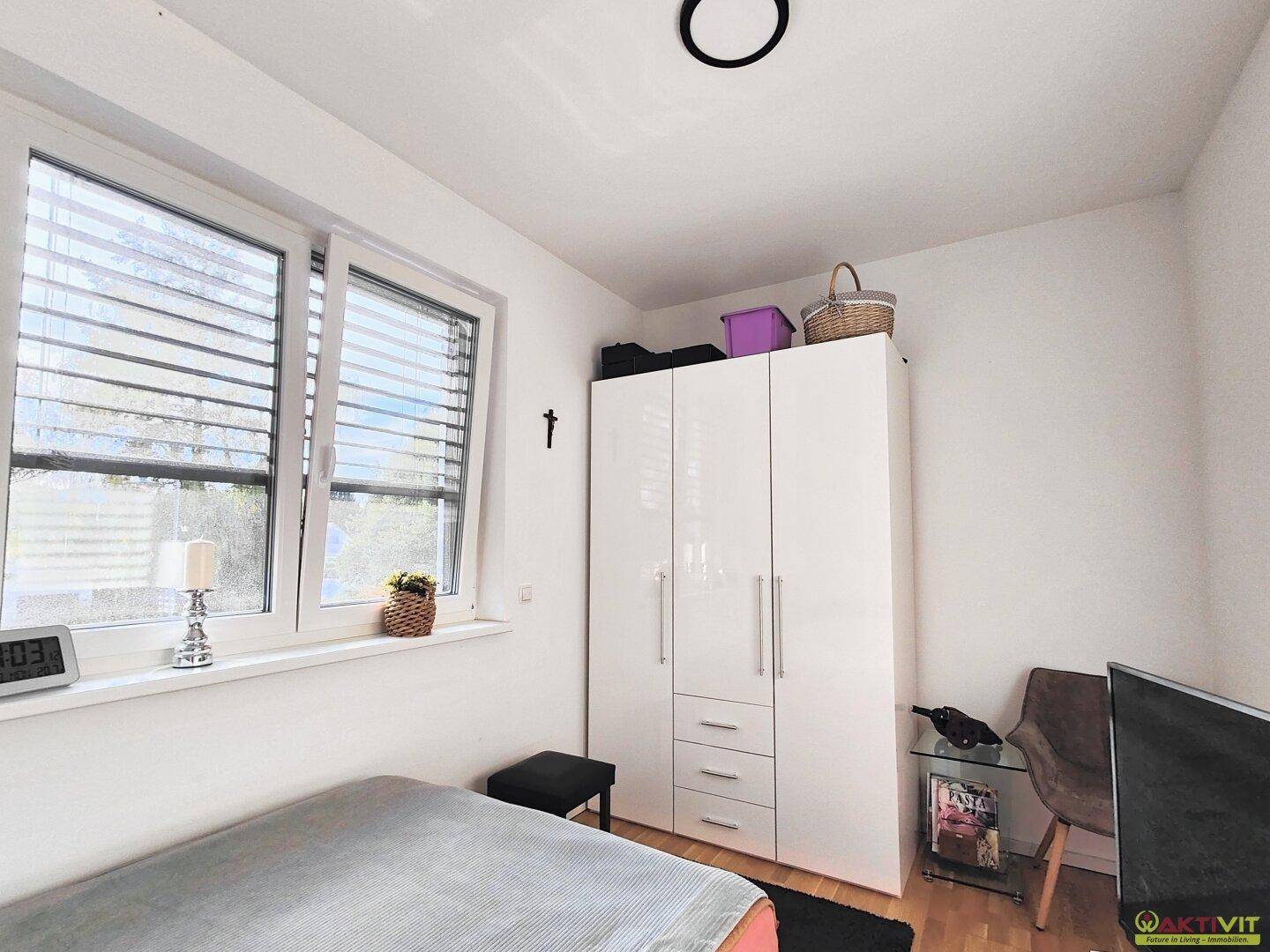Helles Schlafzimmer mit weißem Kleiderschrank, Holzboden und Fenster mit Jalousien.