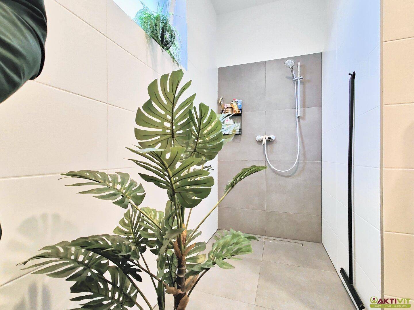 Geräumige Dusche im modernen Badezimmer mit grauen Fliesen und Duscharmatur.