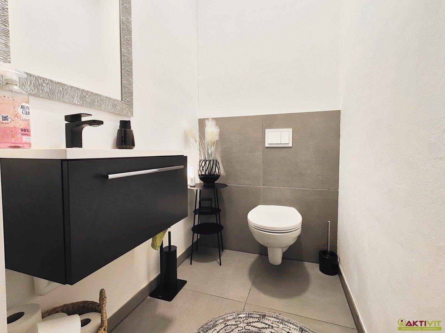 Modernes Gäste-WC mit wandhängender Toilette, schwarzem Waschtisch und Spiegel.