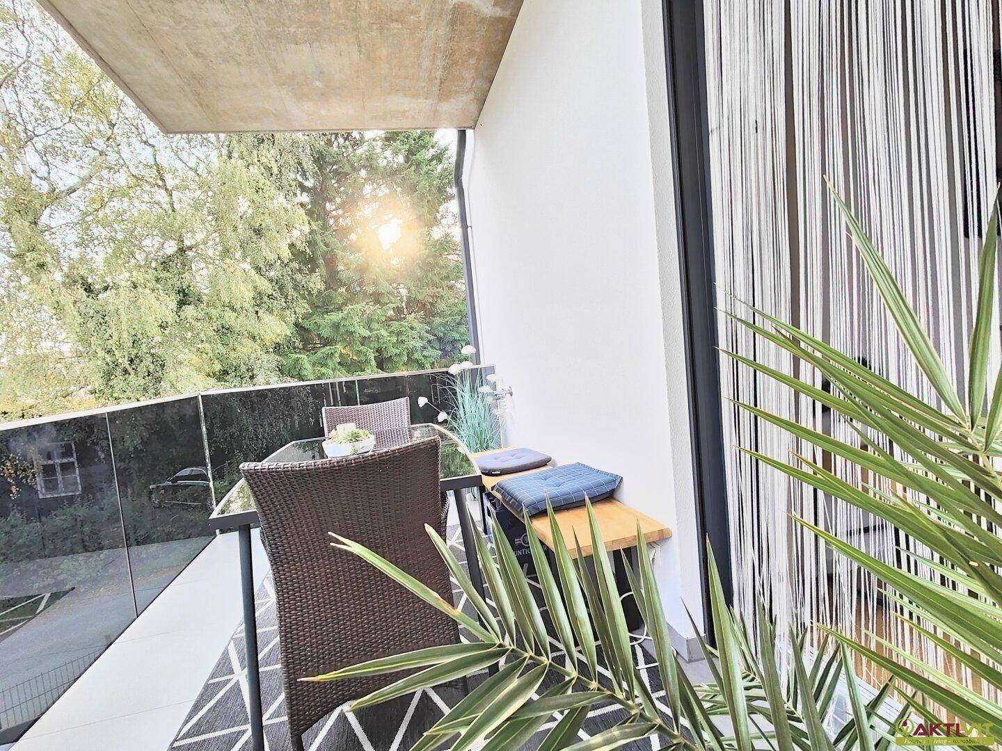 Sonniger Balkon mit Outdoor-Sitzgelegenheiten, Pflanzen und Blick ins Grüne.