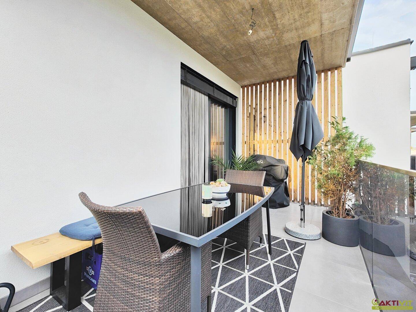 Geräumiger Balkon mit Esstisch, Stühlen und Sonnenschirm, umgeben von einer Holzverkleidung.
