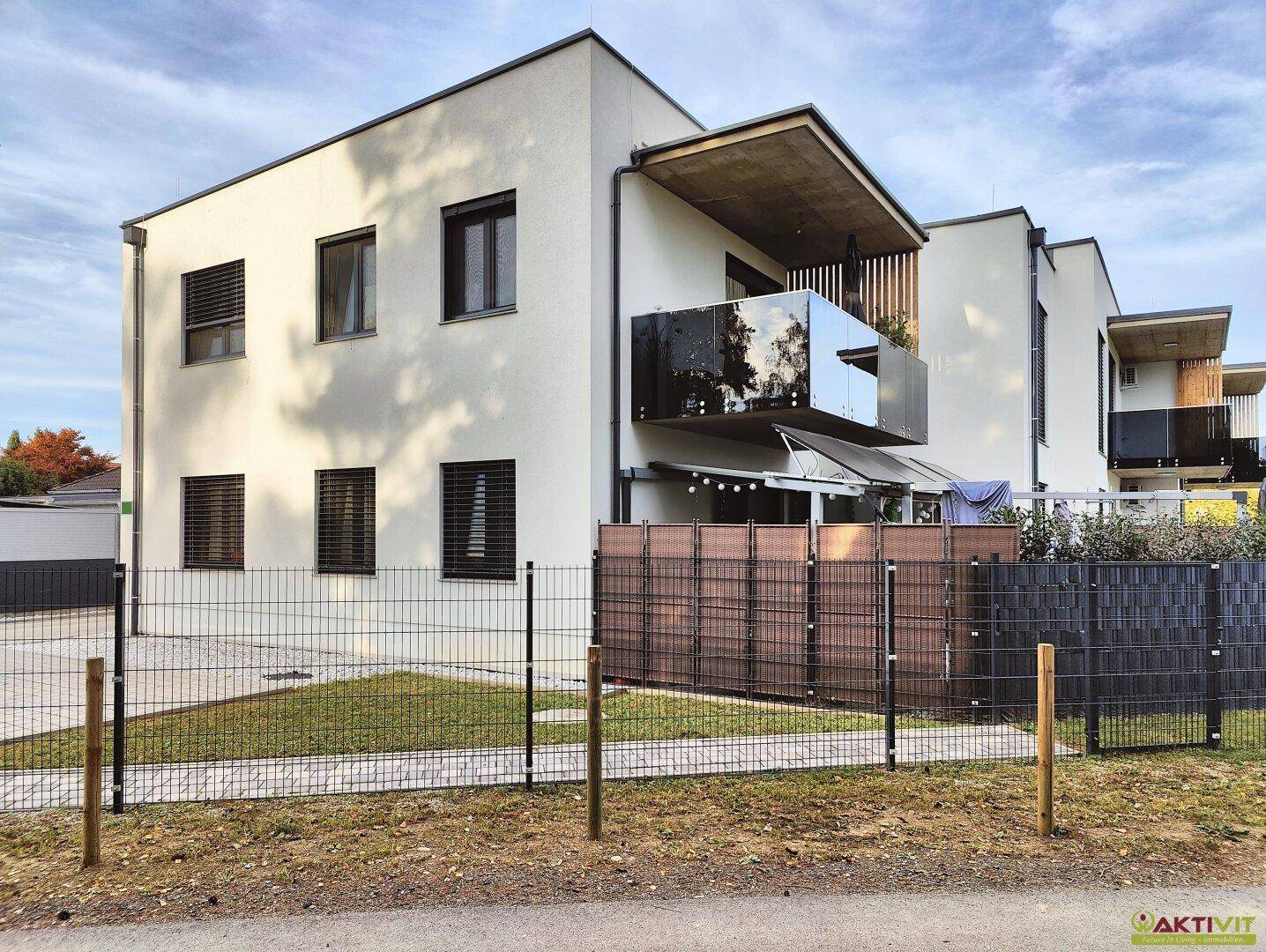 Moderne Wohnanlage mit Balkonen, gepflegtem Rasen und Zaun im Vordergrund.